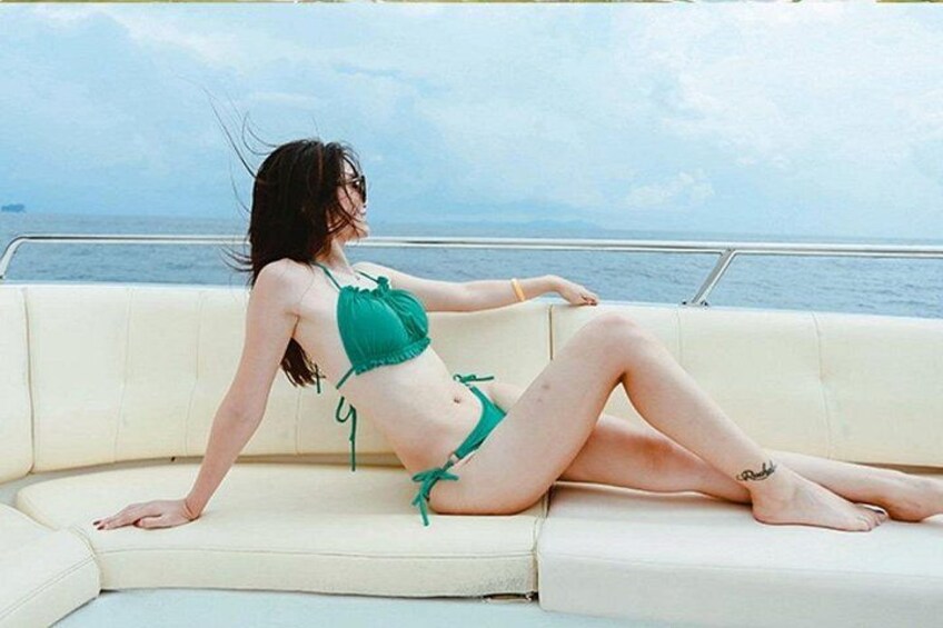 Eine Person in einem grünen Bikini sitzt am Bootsrand, im Hintergrund das Meer. 3