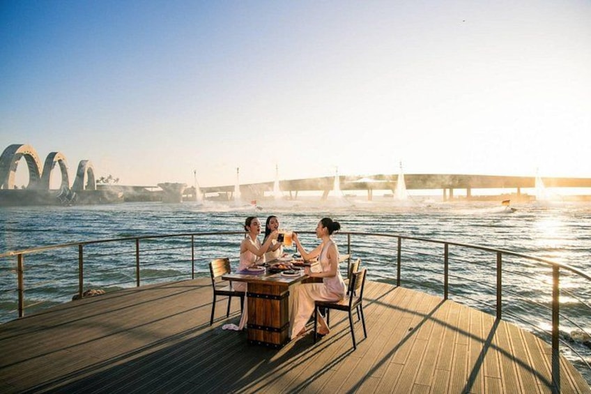 A wooden deck with a table and chairs, overlooking a body of water with a bridge in the background. 2