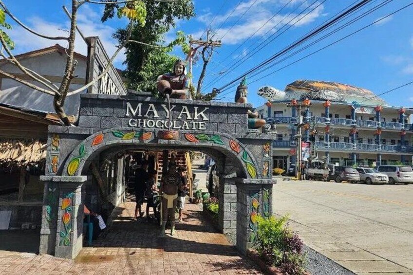 A storefront with a sign reading 'Mayak Chocolate' and a person standing on a balcony. 1