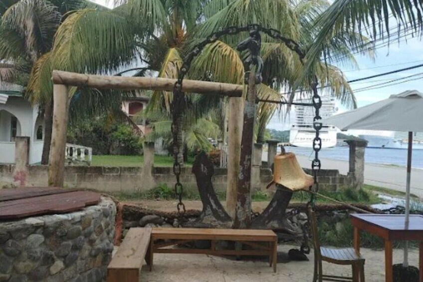A wooden swing set, a bench, and a table in a tropical outdoor setting with palm trees and a beach in the background. 5