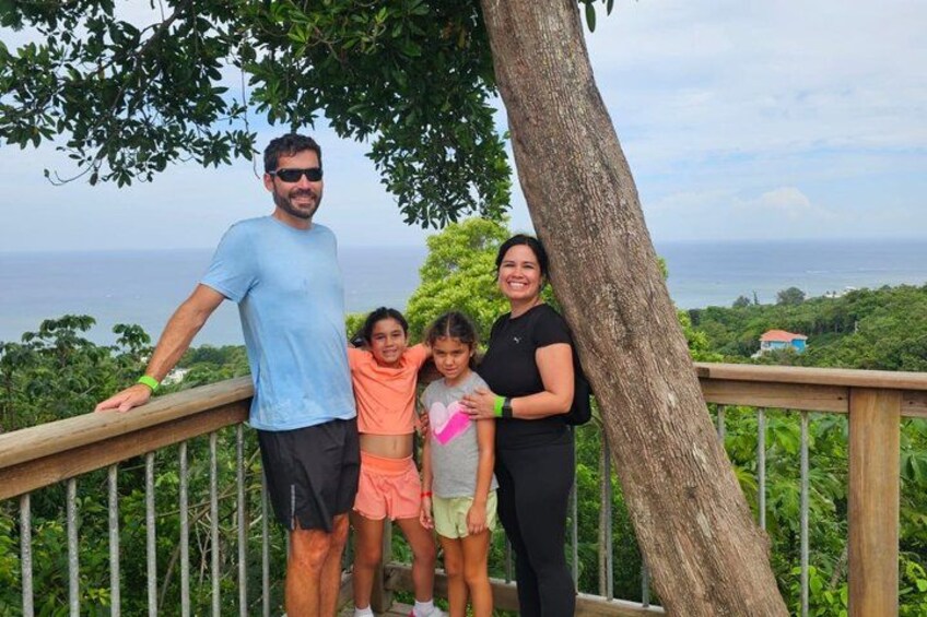 A family on a wooden deck with a tree and ocean view. 3