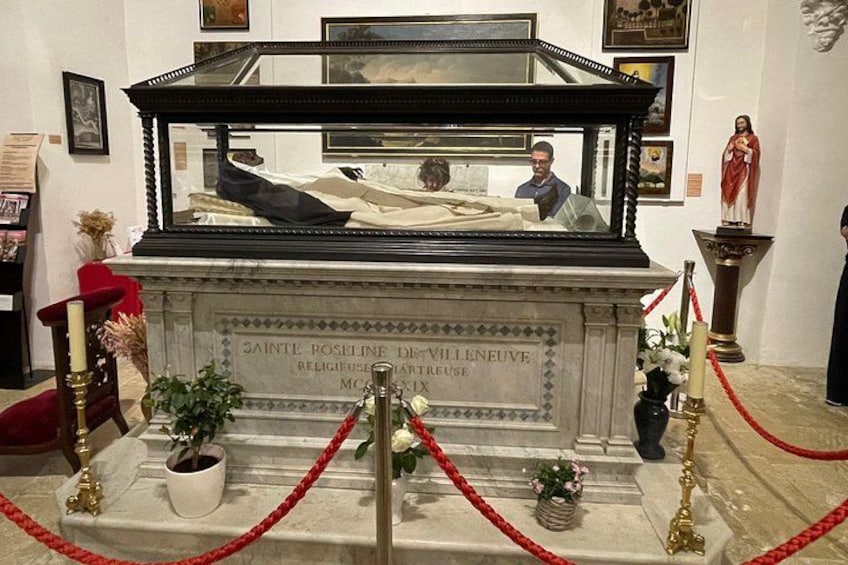 A marble tomb with a glass enclosure, red ropes, and a statue. 3