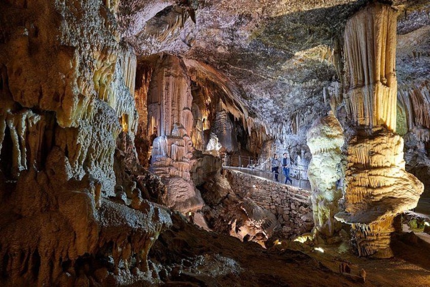 Una grotta con stalattiti e stalagmiti, una persona in piedi e un sentiero. 1