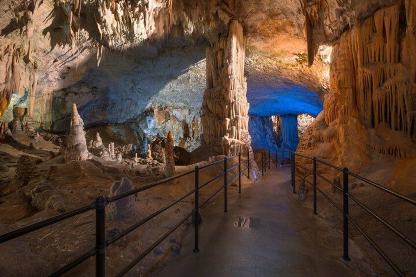 Une grotte ornée de stalactites et de stalagmites, une ouverture bleue menant à une autre grotte, et une rambarde métallique. 2