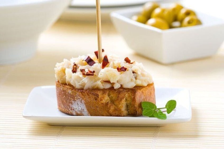 A slice of toast with a creamy spread and bacon bits, garnished with a mint leaf, on a white plate. 3