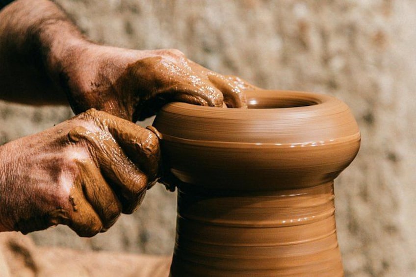 Hands shaping a clay pot on a pottery wheel. 1