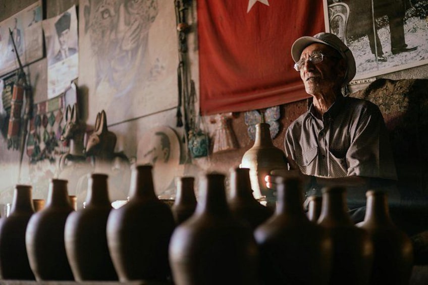 An elderly man in a hat, surrounded by pottery vases. 4
