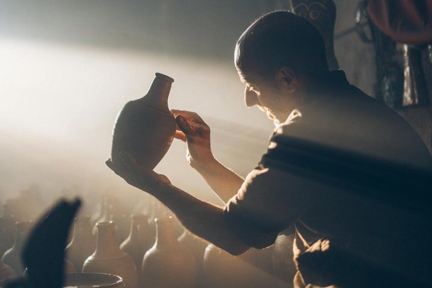 A person holding a clay pot, with a blurred background of similar pots. 5