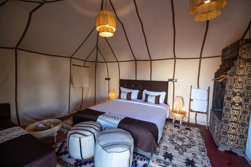 Ein Zeltraum mit einem Bett, Kissen, einer Lampe und einem gemusterten Teppich. 4