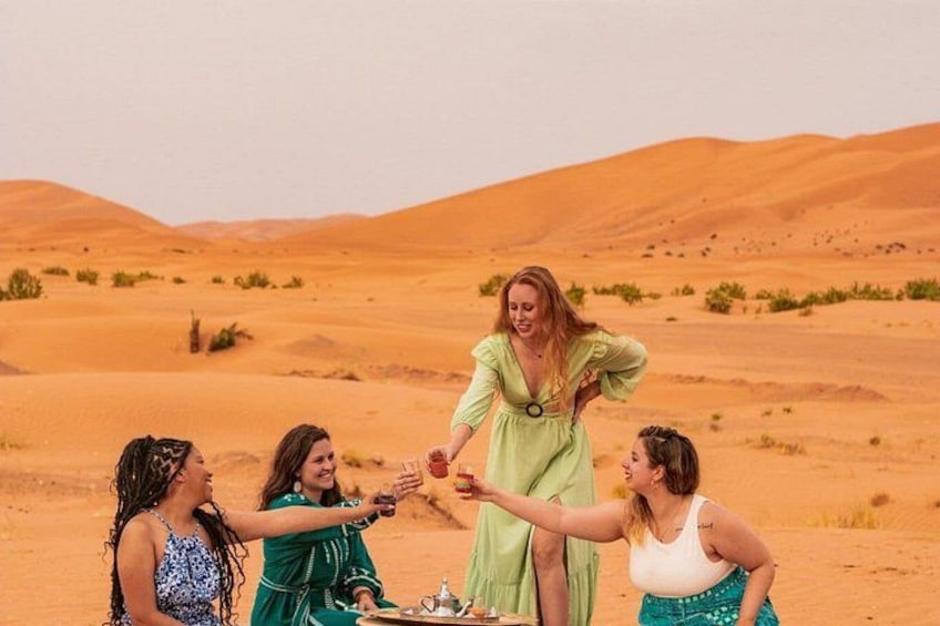 Eine Gruppe von Menschen hält Händchen in einer Wüstenlandschaft, im Hintergrund Sanddünen. 3
