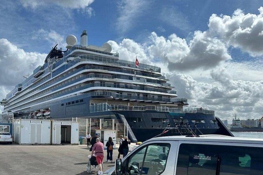 Een groot cruiseschip in de haven, met mensen die er rondlopen en een kleinere boot in de buurt. 3