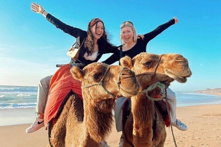 Twee mensen rijden op kamelen aan een strand. 1