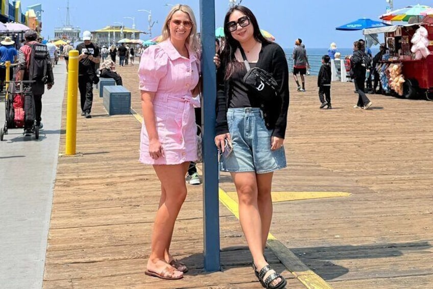 Two people standing on a wooden boardwalk with a beach and umbrellas in the background. 3