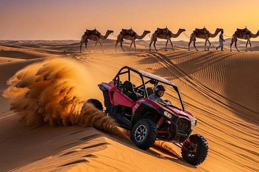 A red off-road vehicle driving through a desert with sand dunes and camels in the background. 1