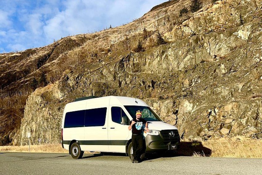 A white van parked on a road with a rocky hillside in the background. 3