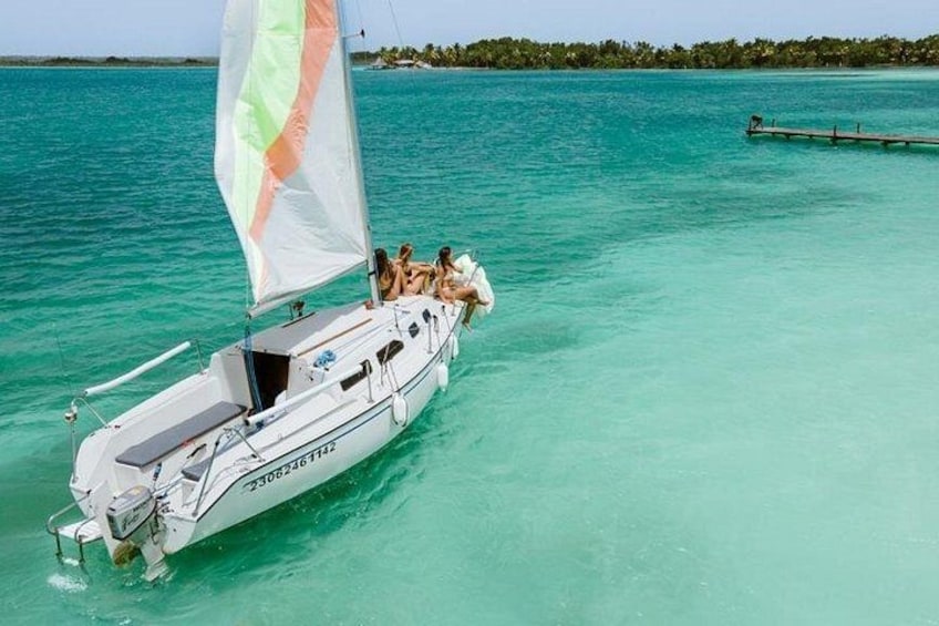 A sailboat with a white hull and a green and orange sail, sailing on turquoise water. 3