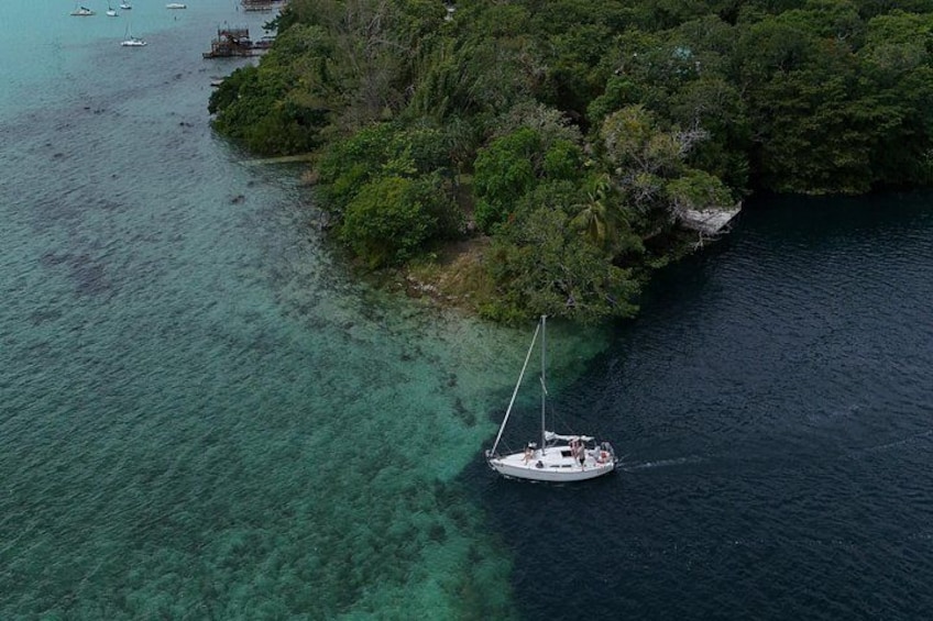 A sailboat anchored near a forested island surrounded by clear waters. 4