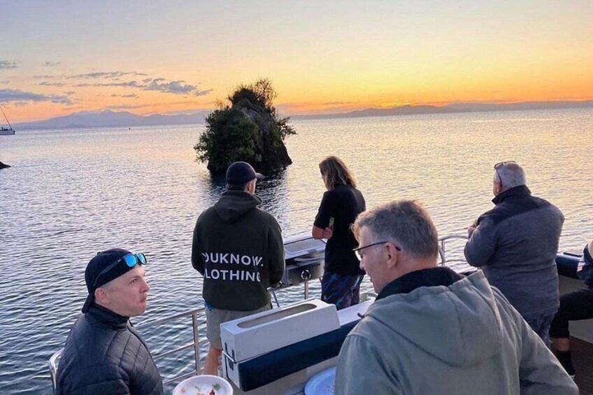 A group of people on a boat during sunset, overlooking a calm body of water with a distant landmass. 4