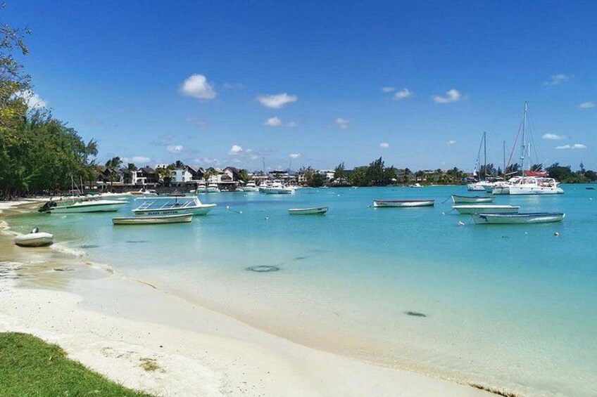 A beach with clear turquoise water, boats, and houses in the background. 2