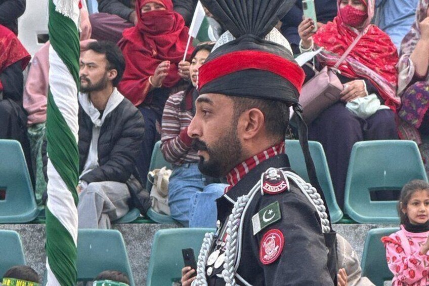 A person in a military uniform with a red fez and a badge, seated in a stadium with spectators. 3