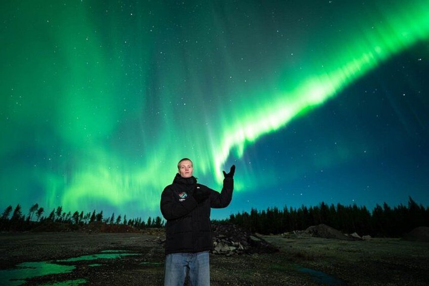 A person standing in a natural landscape with a green aurora display in the sky. 2
