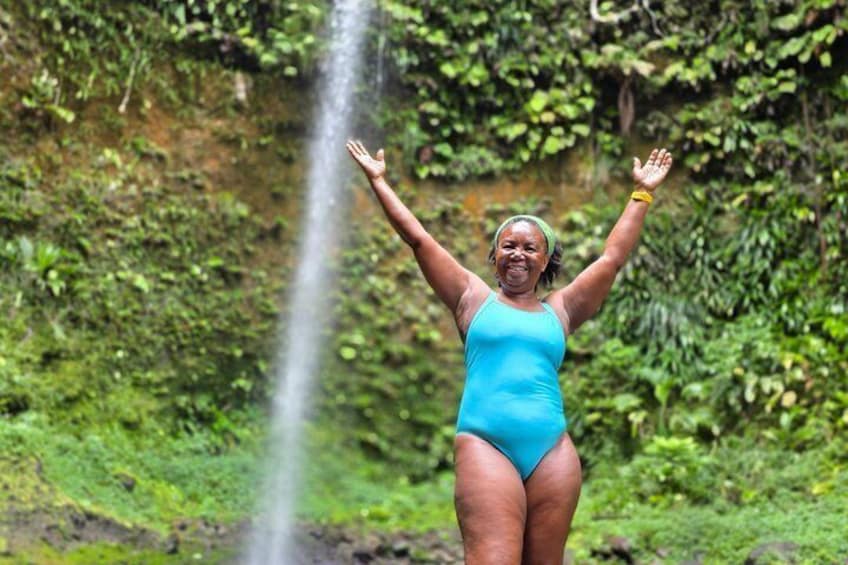 Une personne vêtue d’un maillot de bain bleu, debout devant une cascade, les bras levés. 5