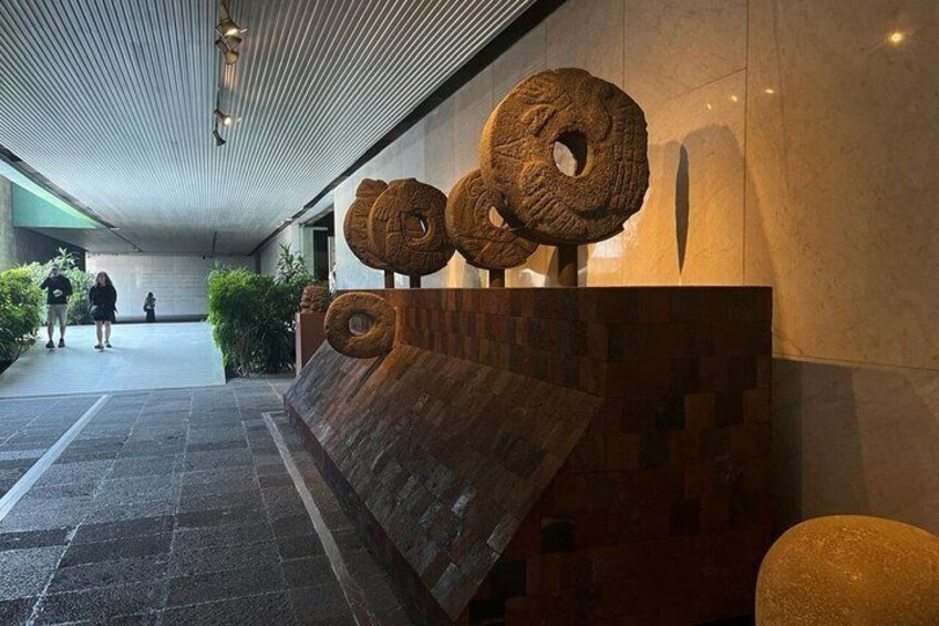 En modern entré till en byggnad med en unik träbänk och stora, cirkelformade skulpturer. 3
