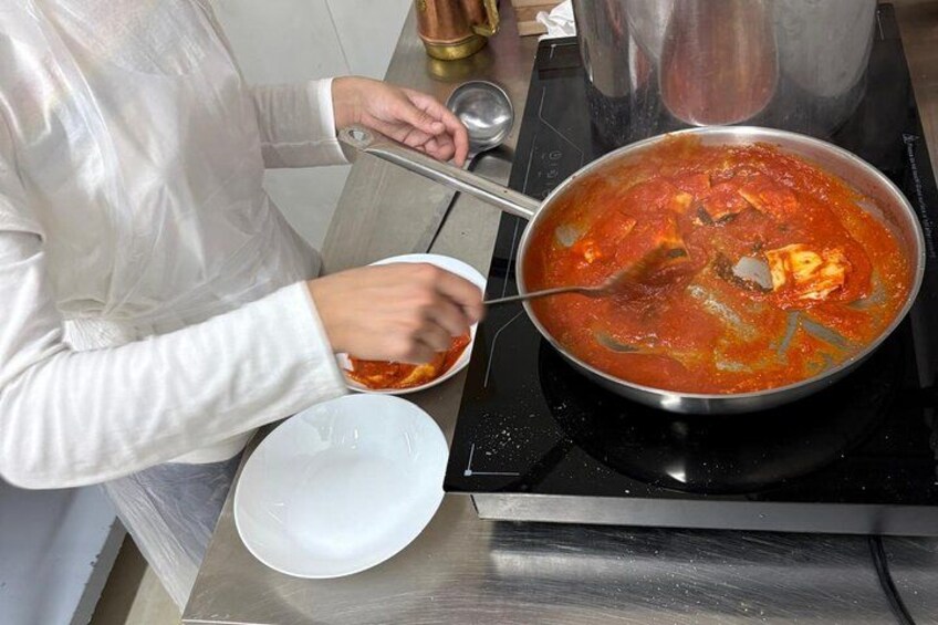 A person cooking a red sauce in a pan on a stove. 2