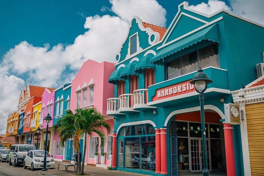 Una calle colorida con edificios, una palmera y coches estacionados. 3
