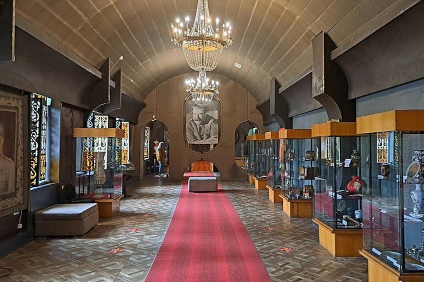 An interior with a red carpet, chandeliers, and glass display cases with artifacts. 4