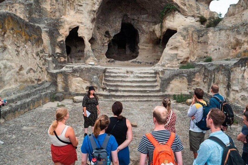 A group of people observing a cave entrance with steps leading up to it. 1