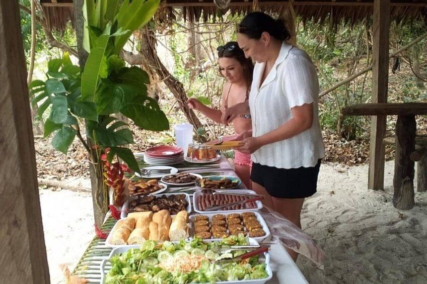 A picnic setup with food and drinks on a table, surrounded by natural scenery. 3