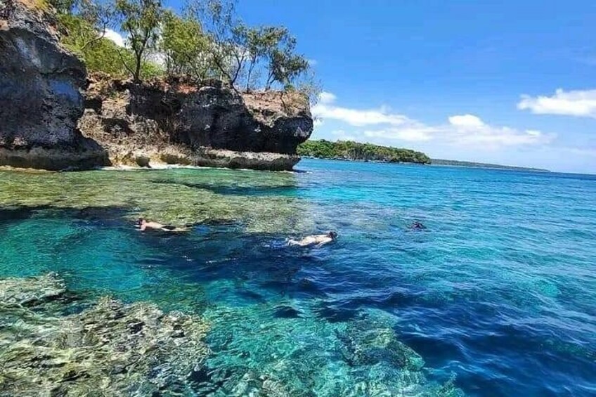 A clear blue sea, rocky shore, and a person swimming. 4