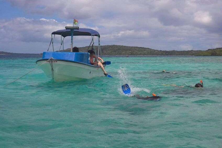 A boat with a person steering, another person swimming, and a third person on a surfboard in the water. 1