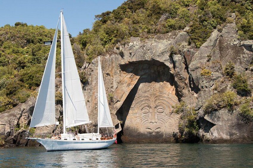 Un velero con dos velas, una costa rocosa y una pared rocosa tallada. 1