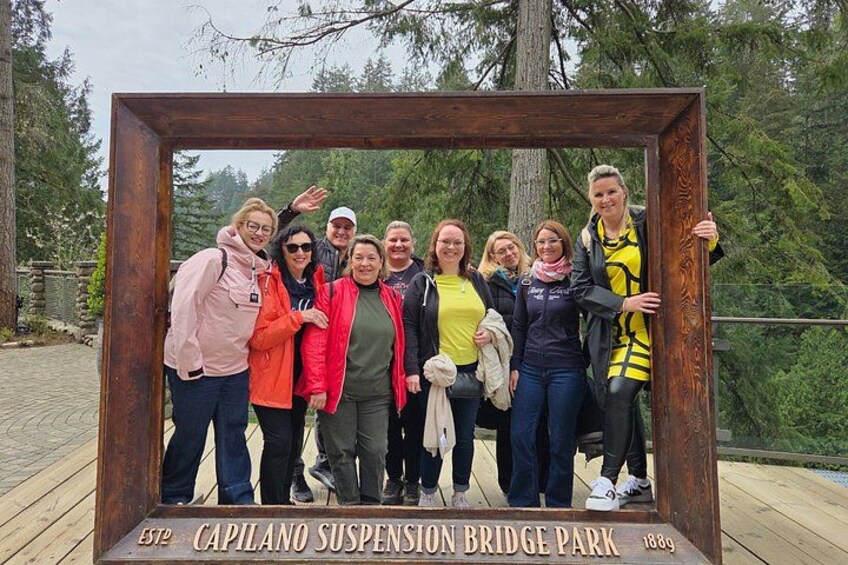 Un grupo de personas posando frente a un letrero de madera en el Parque del Puente Colgante de Capilano. 3