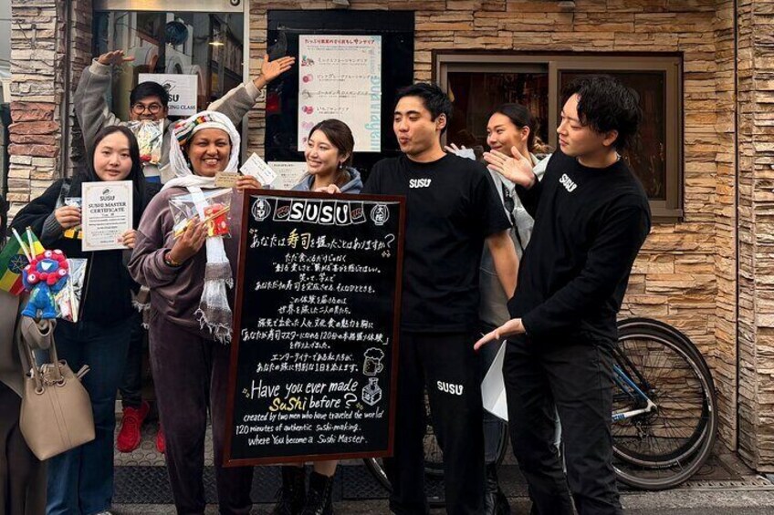 A group of people holding certificates and a sign with Japanese text, standing in front of a building with a stone facade. 4