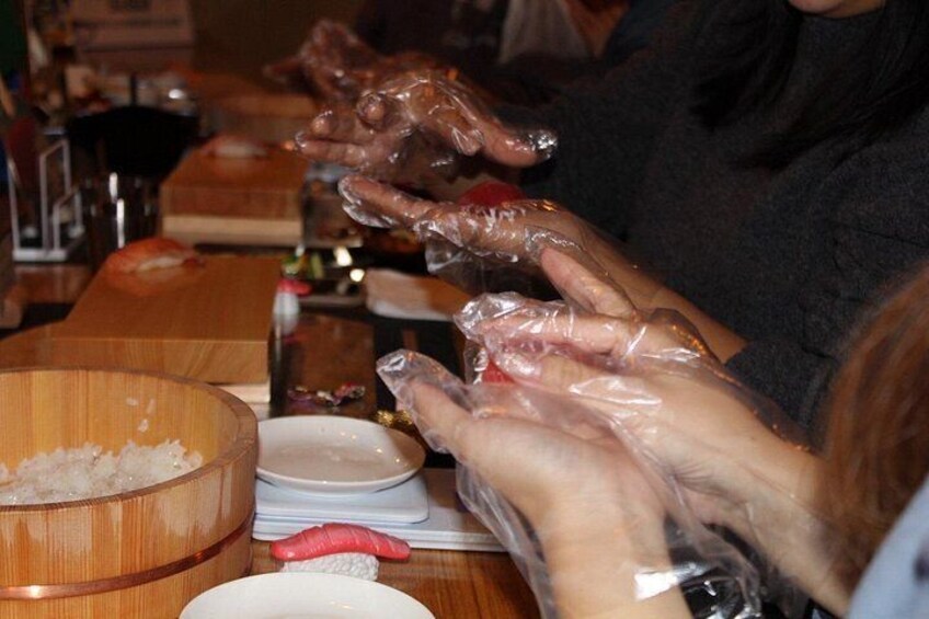 Hands wearing plastic gloves handling food items on a wooden table. 4