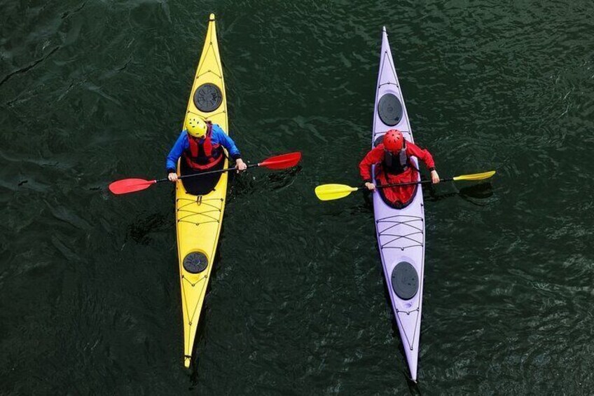 Two kayakers in yellow and red kayaks paddling on a body of water. 3