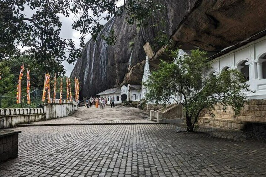 A cobblestone pathway leading to a white building with a large rock formation in the background. 5