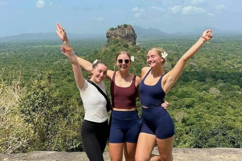 Three people standing on a ledge with a mountainous landscape in the background. 1
