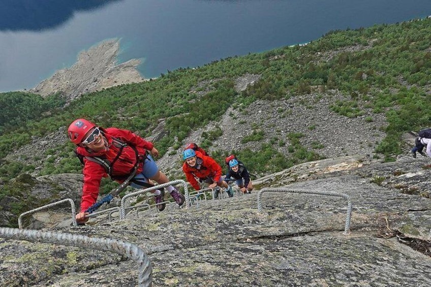 Hikers climbing a rocky mountain path with a clear sky and a distant rocky outcrop. 3