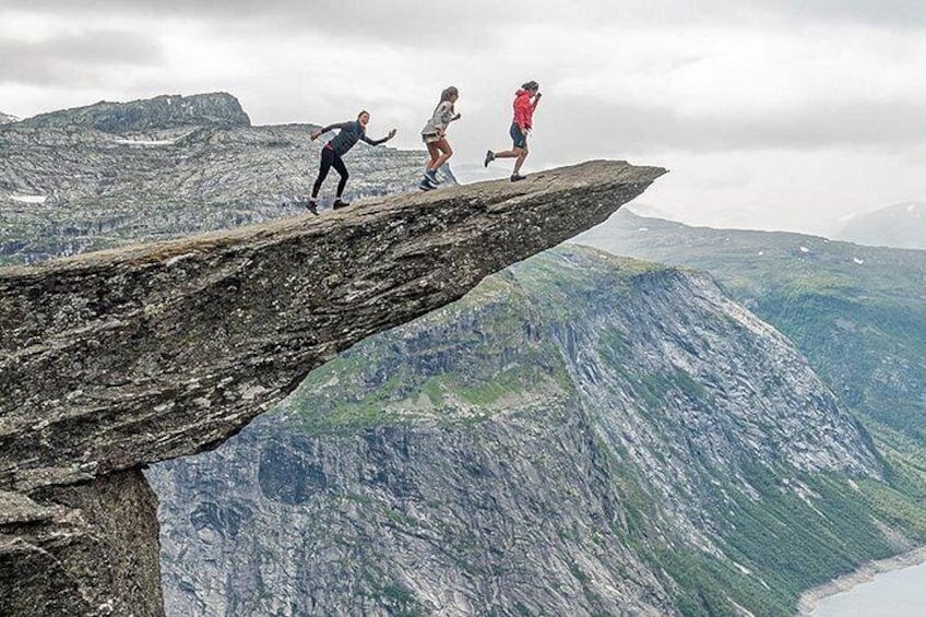 Three people on a narrow ledge with a mountainous landscape in the background. 5