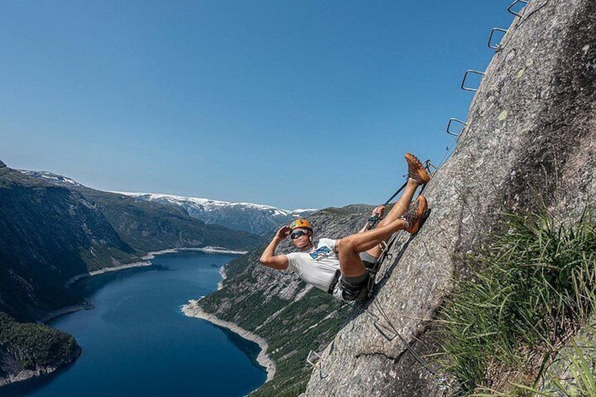 A person rappelling down a steep cliff with a lake and mountains in the background. 4