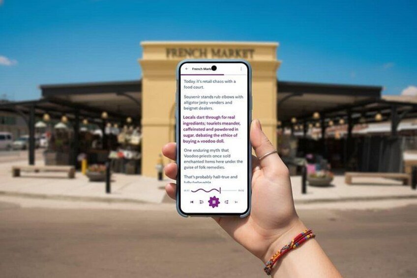A hand holding a smartphone with text on the screen, in front of a building labeled 'FRENCH MARKET'. 1