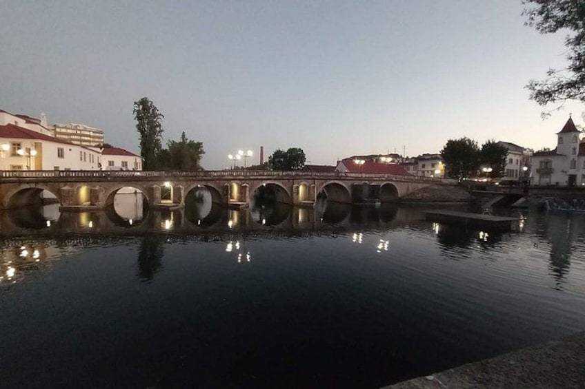 A calm river with a stone bridge and buildings in the background. 2