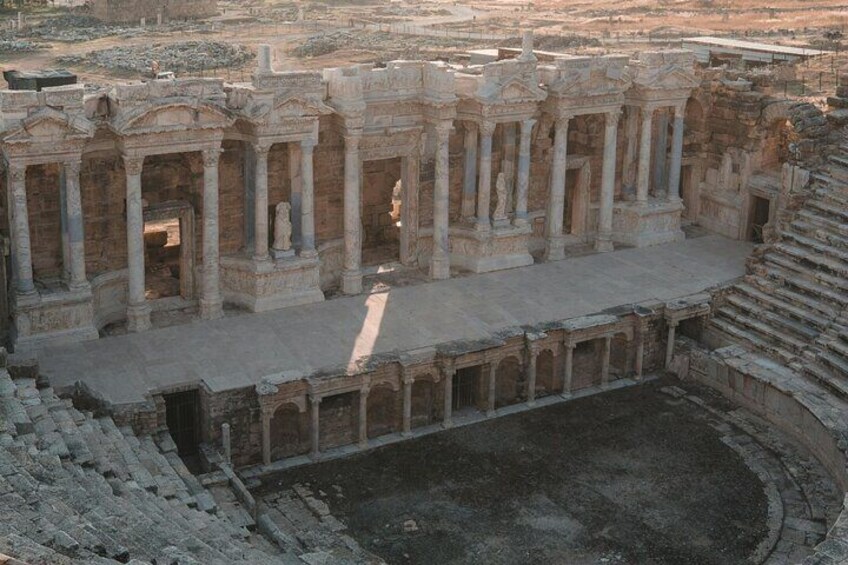 An ancient amphitheater with stone columns and a central stage. 4