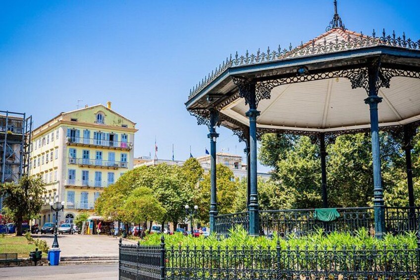 Ein Pavillon mit aufwendiger Metallverzierung, ein Gebäude mit Balkonen und ein klarer, blauer Himmel. 4