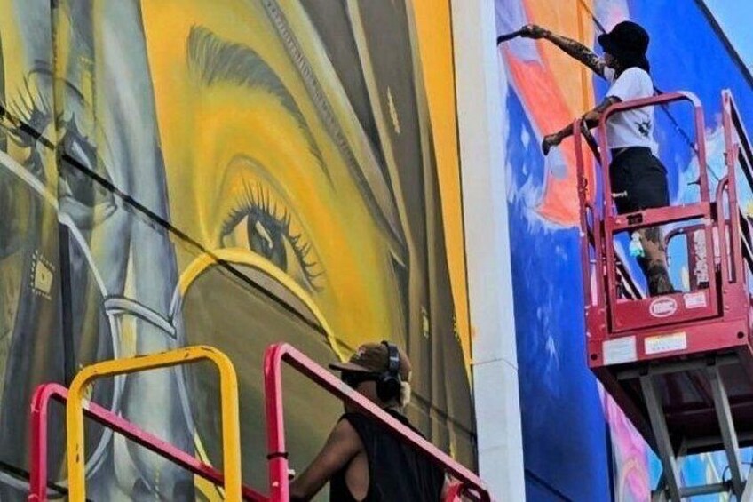 Une fresque est en cours de réalisation sur un mur, avec une échelle et une personne sur une plateforme. 2