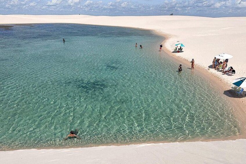 En strand med kristallklart turkost vatten, där folk badar och solar, och en sandstrand. 1